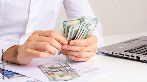 caucasian hands counting dollar banknotes on white wooden surface