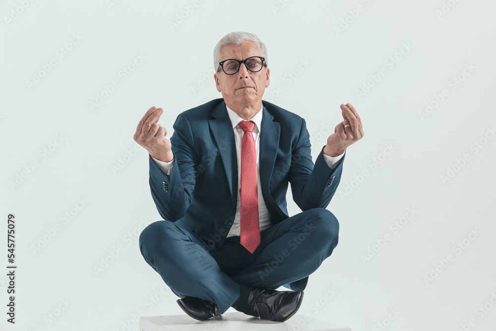 old man in his 60s in a turkish pose holding elbows on knees and meditating