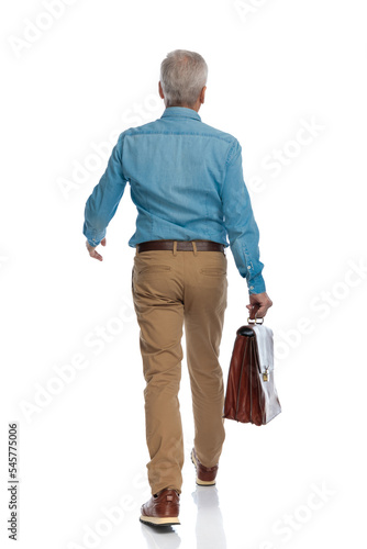 back view of casual man in his 60s with suitcase walking
