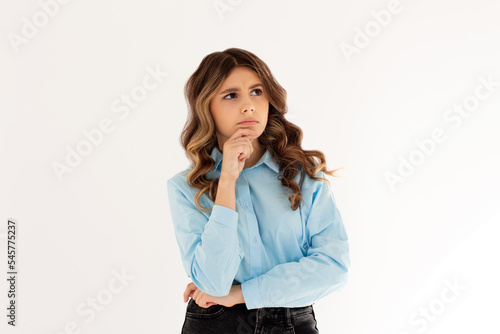 Thoughtful woman keeps hand on chin looks pensively above dressed in casual blue shirt poses against white background blank copy space for your advertising content thinks about future