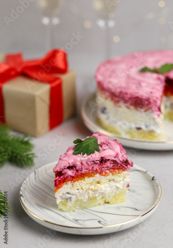 Traditional Russian New Year's salad. A portion of puff salad herring under a fur coat on a white plate. Russian national cuisine. Selective focus.