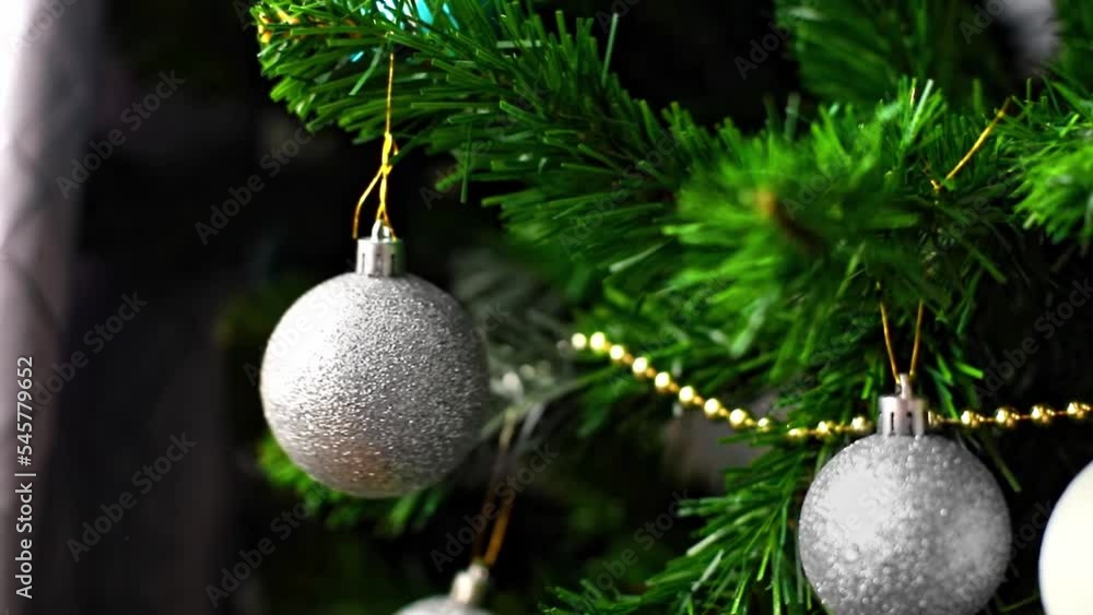 Close up moving Christmas toy of silver color on a Christmas tree branch in the house