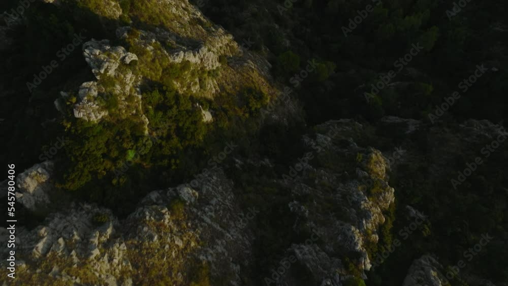 Forwards fly above rocks and green vegetation lit by low sun. High angle view of natural scene, revealing road winding. Amalfi, Italy Forwards fly above rocks and green vegetation lit by low sun. High angle view of natural scene, revealing road winding. Amalfi, Italy