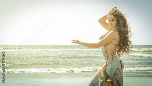 A bellydance dancer dancing to arabic music in front of a beach photo