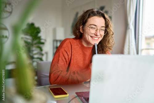 Happy young woman using laptop sitting at desk writing notes while watching webinar, studying online, looking at pc screen learning web classes or having virtual call meeting remote working from home.