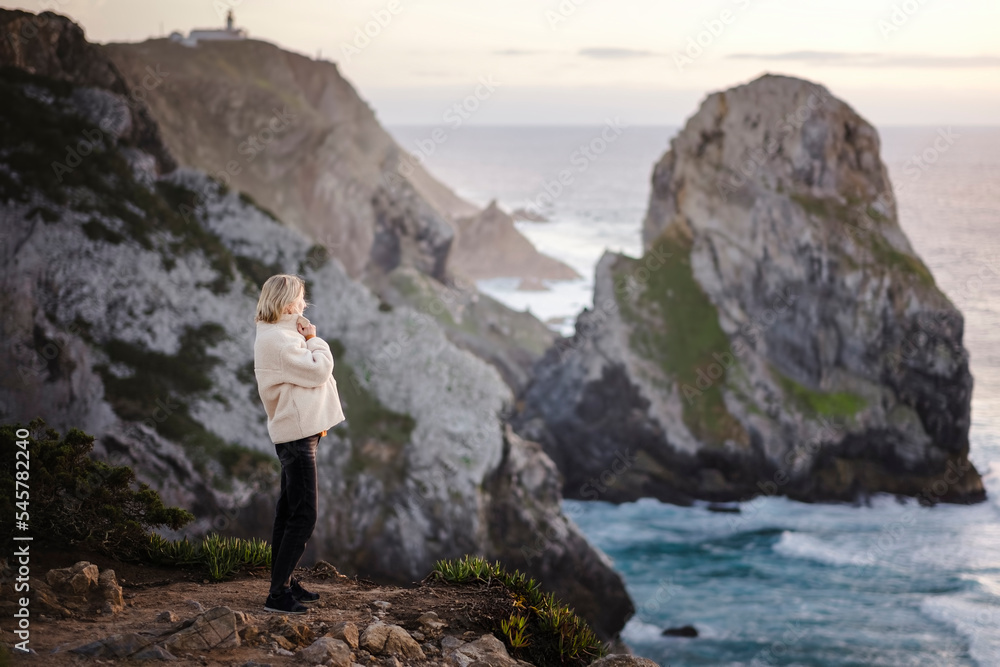 A woman standing against the rock of Cape Roca. Sintra, Portugal.