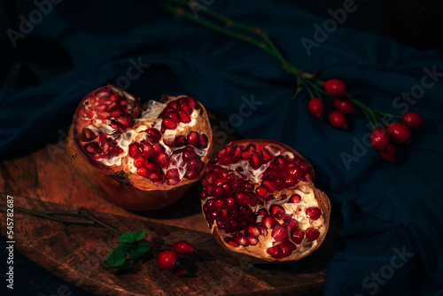 Pomegranate on a cutting board and rosehip branches on black table. Still life. Closeup