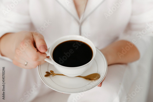 Cozy woman in pajamas holding a cup of hot coffee while relaxing at home