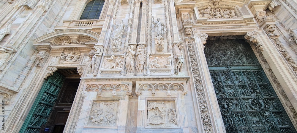 Cathedral Duomo di Milano. Panoramic view of the ornate facade with many marble sculptures on the wall. Entrance to the cathedral of European country. Detail of a building.