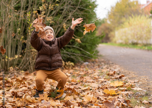 A little boy jumps in the autumn foliage and throws up the leaves