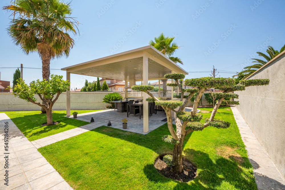 Garden with gazebo with rattan tables and chairs and artistically pruned trees