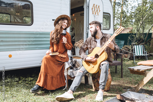 Young beautiful loving couple travelling across country in the van. Millennial man and woman in a travel camper. Cozy atmosphere, vacations vibe. Drinking tea, playing guitar