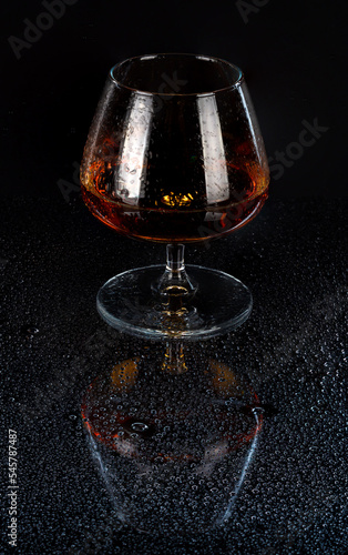 фотографія filled cognac glass reflected from mirror surface with dew water droplets dark b