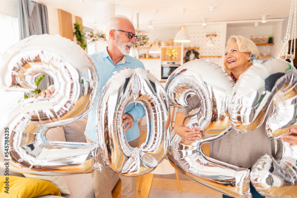 Senior couple holding balloons shaped as numbers 2023
