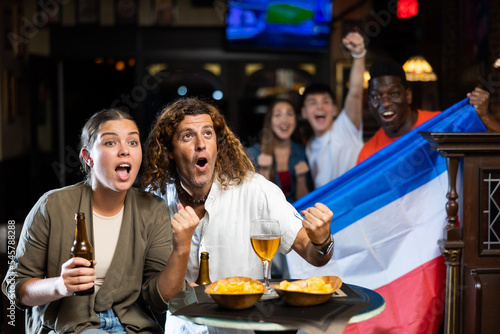 Fans with flag of Netherlands celebrate victory of their favorite team in a beer bar