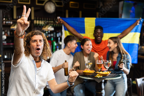 Cheerful proud football fan gesturing emotionally after goal scored by favorite team while watching championship match on TV in sports bar 