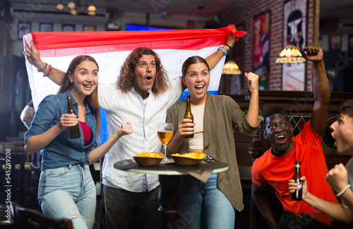 Fans with flag of Netherlands celebrate victory of their favorite team in a beer bar