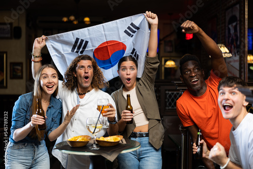 Group of happy fans celebrate victory of their favorite team with flag of South Korea in a beer bar