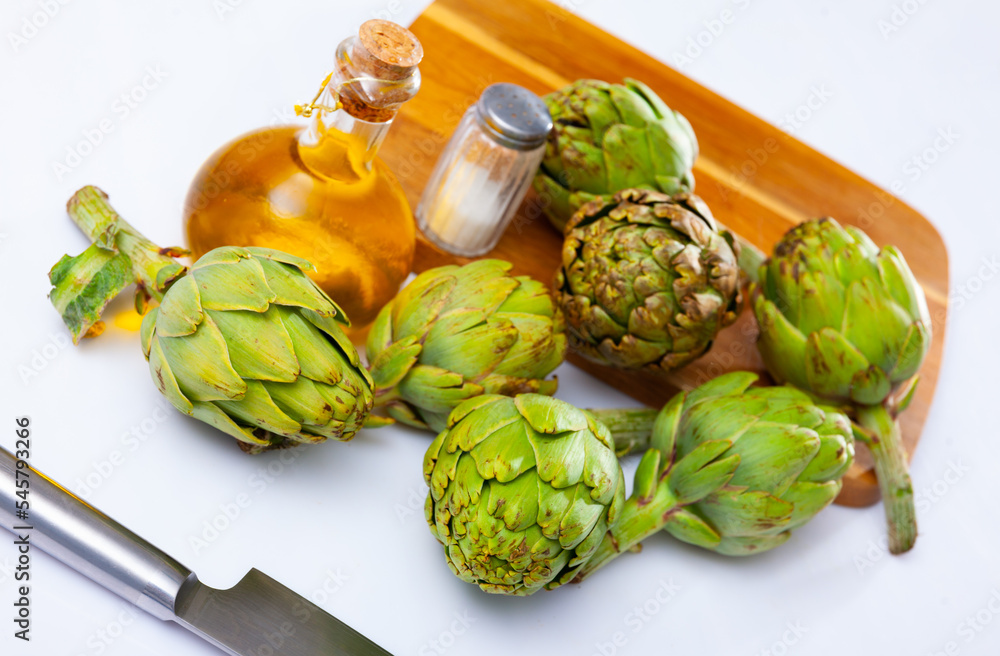 Fototapeta premium Bunch of artichokes placed over white background with saltcellar and glass oil bottle.