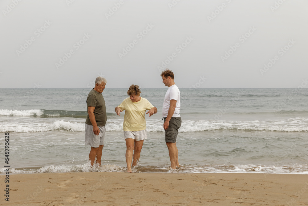 Elderly parents with an adult son walking by the sea, a healthy lifestyle, taking care of the family