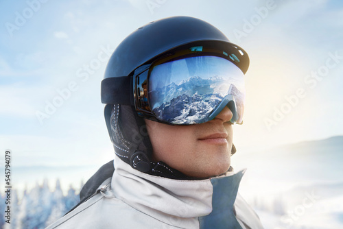 Close Up Of The Ski Goggles Of A Man With The Reflection Of Snowed Mountains. Man In The Background Blue Sky. Winter Sports