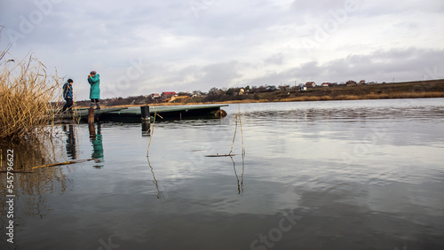 A man stands on a pier on the lake against the backdrop of the village  