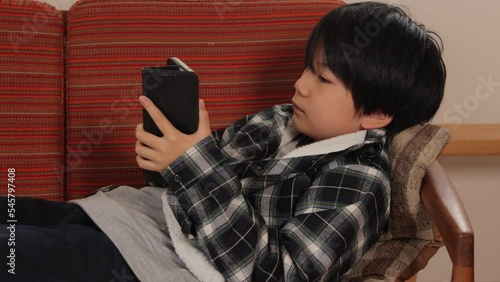 Asian teenage boy playing online game with his smartphone on the couch.