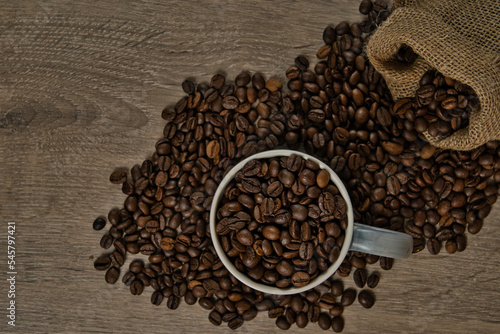 Top view of brown roasted coffee beans spilled on a table with a full coffee mug