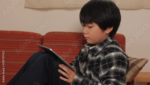 Japanese teenage boy watching online video with his digital tablet on the couch.