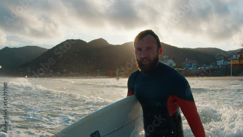 Portrait of the man surfer walking into the ocean with surfing board