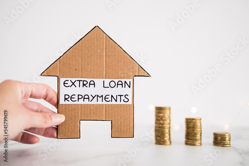 extra loan payment text on cardboard house  in front of decreasing stacks of coins, paying down your loan or mortgage in advance photo