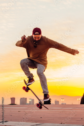 Guy jumping in the air with his skateboard with amazing sunset in the background.