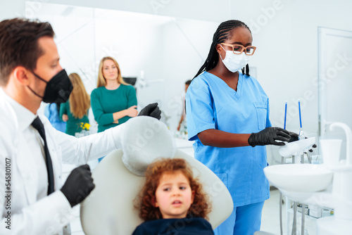 Assistant preparing tools for dentist with patient.