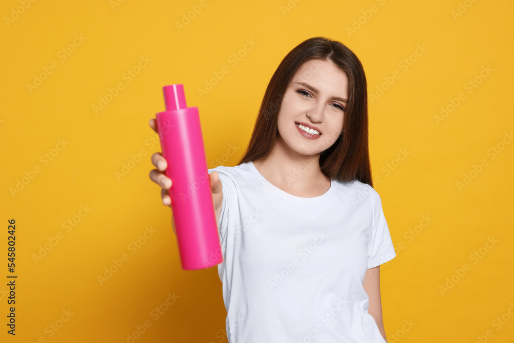Beautiful young woman holding bottle of shampoo on yellow background Beautiful young woman holding bottle of shampoo on yellow background