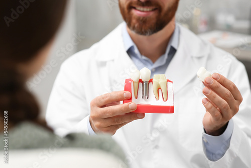 Doctor with educational model of dental implant consulting patient in clinic, closeup