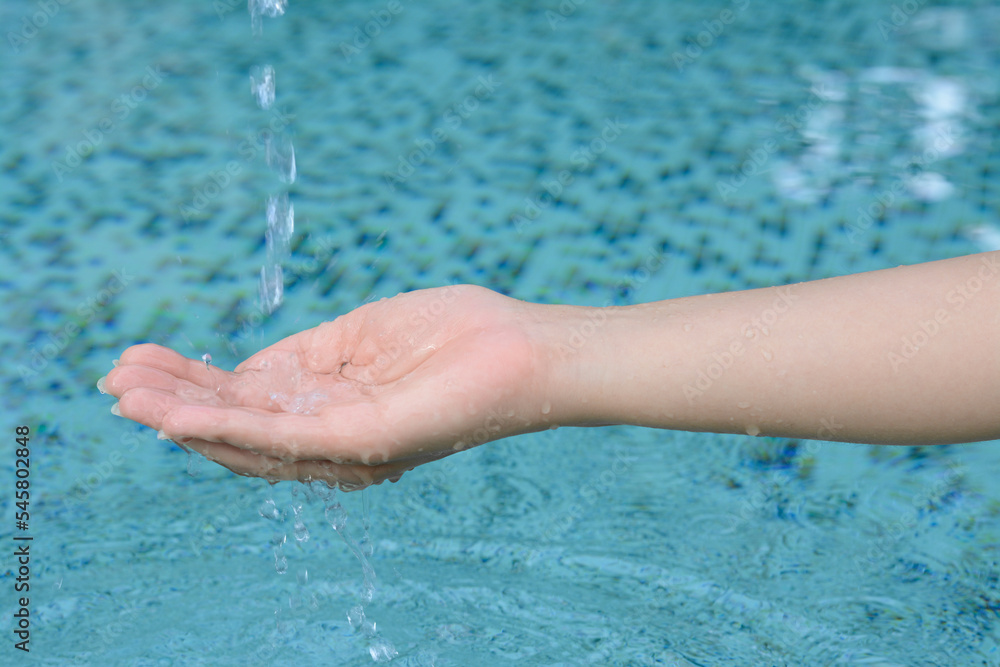 Water pouring into the girl's hand above pool, closeup