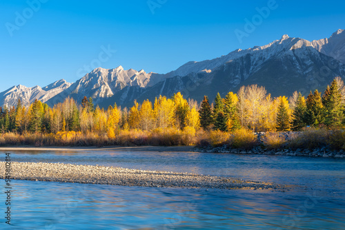 Landscape during sunrise. Autumn trees on the river bank. Mountains and forest. Reflections on the surface of the river. Vivid colours during dawn. Natural landscape. Alberta, Canada.