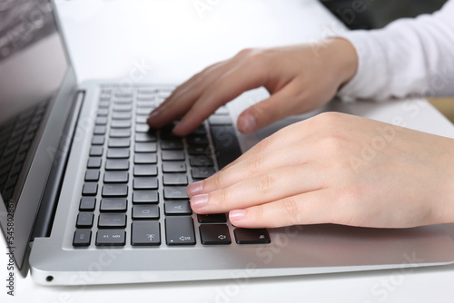 Woman working on laptop at white table in office, closeup