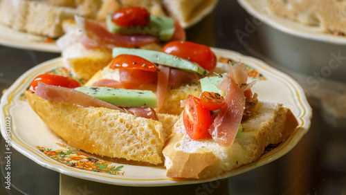 Close-up of plate with bruschetta of bread, prosciutto, cheese with herbs and cherry tomatoes
