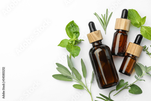 Bottles of essential oil and fresh herbs on white background, flat lay. Space for text