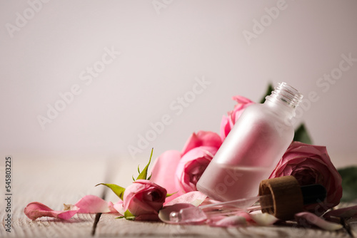 Bottle of essential oil and roses on white wooden table against light background. Space for text photo