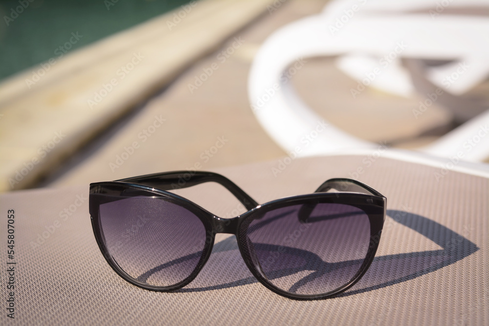 Stylish sunglasses on grey sunbed outdoors. Beach accessory, closeup