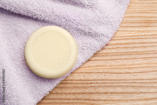 Solid shampoo bar and towel on wooden table, top view. Space for text