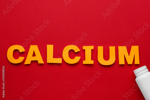 Word Calcium made of orange letters and open bottle on red background, flat lay