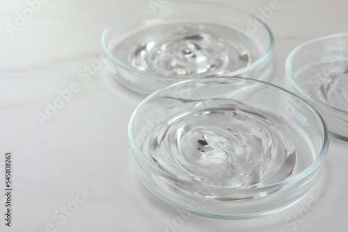 Petri dishes with liquids on white marble table, closeup. Space for text