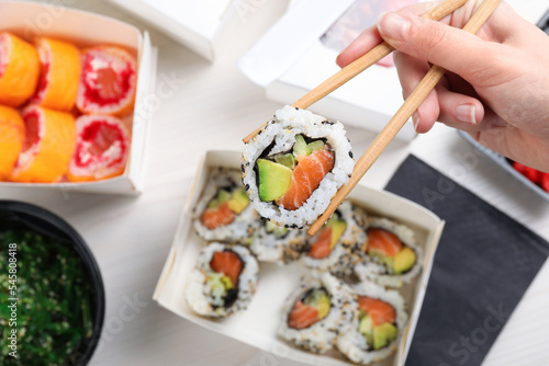 Woman eating sushi rolls with chopsticks at white table, top view