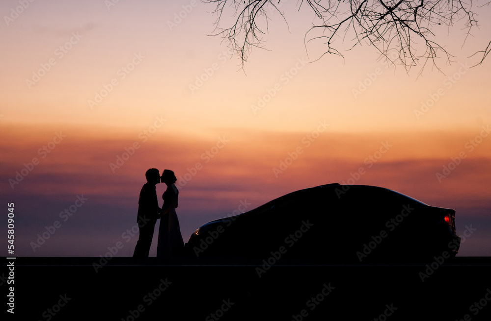 silhouette of a wedding couple in love at sunset near the car.