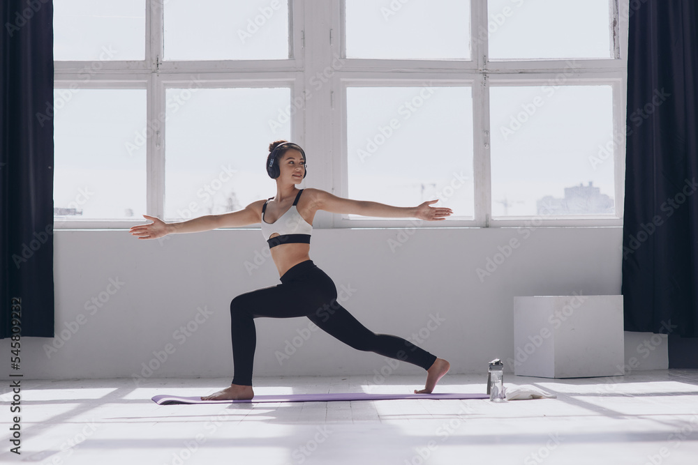 Fit young woman doing stretching exercises while practicing in front of the window