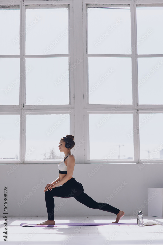 Confident young woman doing stretching exercises while practicing in front of the window