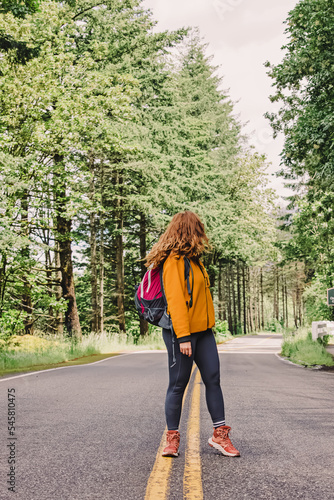 Woman hiker with a backpack standing on the road through the park of forest